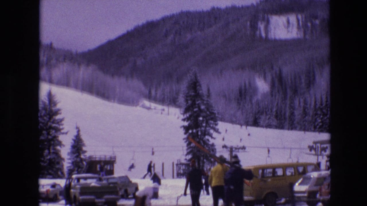 Vail, Colorado ski-resort base area in 1974 with skiers on a snowy slope, people in winter coats, parked cars, and a yellow station wagon in the foreground.
