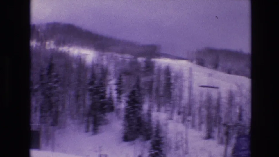 Soft handheld 8mm view of Vail, Colorado ski slopes in 1974, showing snowy runs, evergreen trees, bare trees, lift hardware, and small distant skiers.