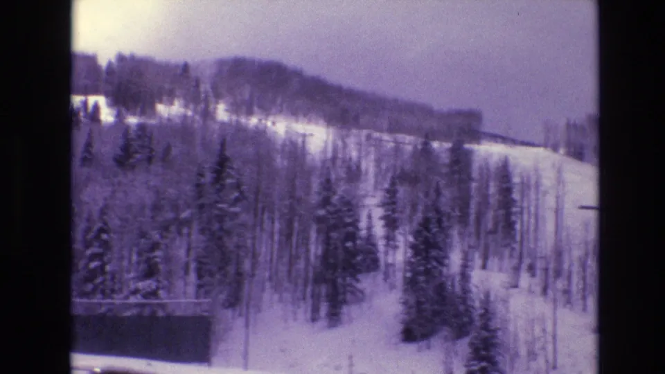 1974 Vail, Colorado 8mm frame showing snow-covered evergreens and a wooded mountain slope in soft purple-blue winter light.