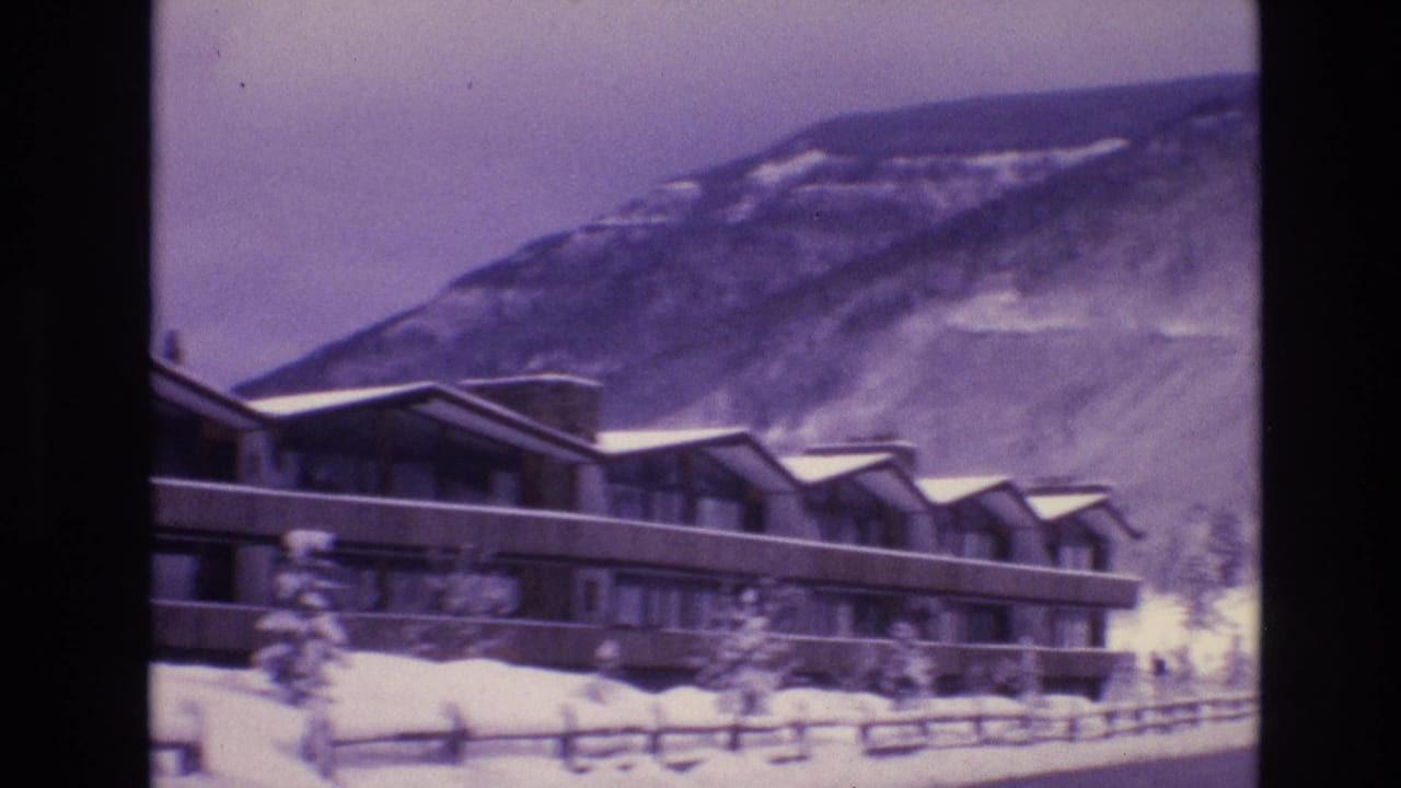 Long lodge facade behind snow and a wooden fence.