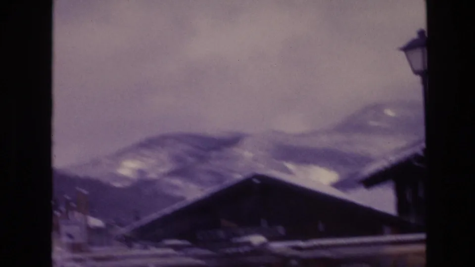 1974 Vail, Colorado 8mm frame showing a dark lodge roofline, snow-covered mountain slopes, a lamp post, nearby building edge, and muted winter light.