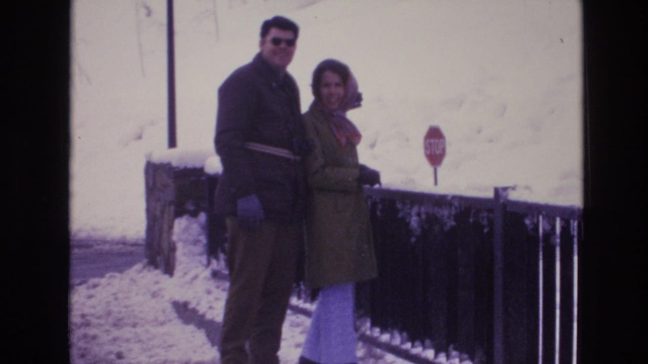 In Vail, Colorado in 1974, an adult couple poses beside a snow-covered railing, with a red stop sign and snowy hillside in the background.