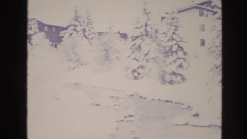 1974 Vail, Colorado home-movie frame of a bright snowy creek area with evergreen trees and lodge buildings partly washed by exposure.