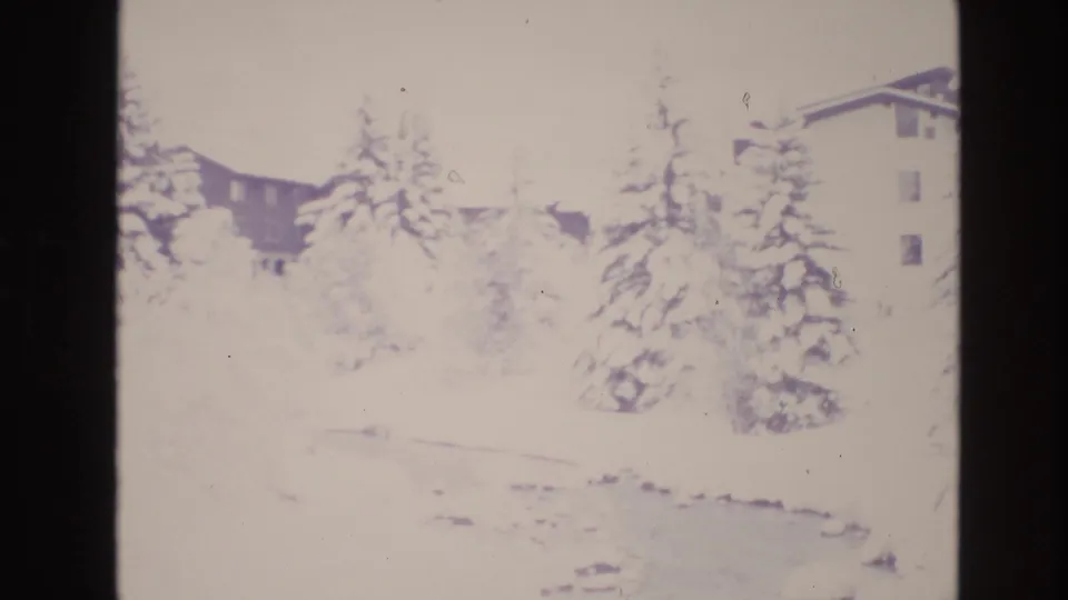 1974 Vail, Colorado frame showing a pale, snowy stream corridor with evergreens and alpine buildings in the lodge area.