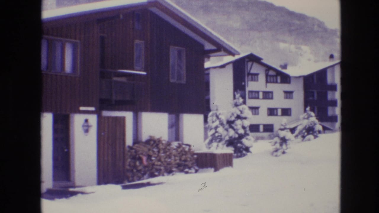 1974 Vail, Colorado 8mm frame showing dark wood resort buildings, snow-covered roofs, foreground snow, and a pale mountain backdrop.