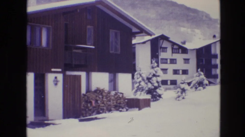 1974 Vail, Colorado 8mm frame showing dark wood resort buildings, snow-covered roofs, foreground snow, and a pale mountain backdrop.