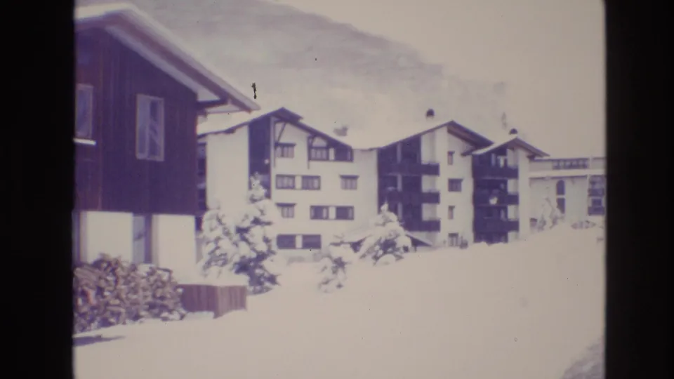 1974 Vail, Colorado frame with chalet-style apartment blocks, dark balconies, snow-laden trees, and bright winter snow across the foreground.