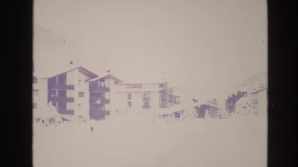 1974 Vail, Colorado frame with resort apartment blocks partly washed by bright snow exposure, distant evergreens, and a faint mountain edge.