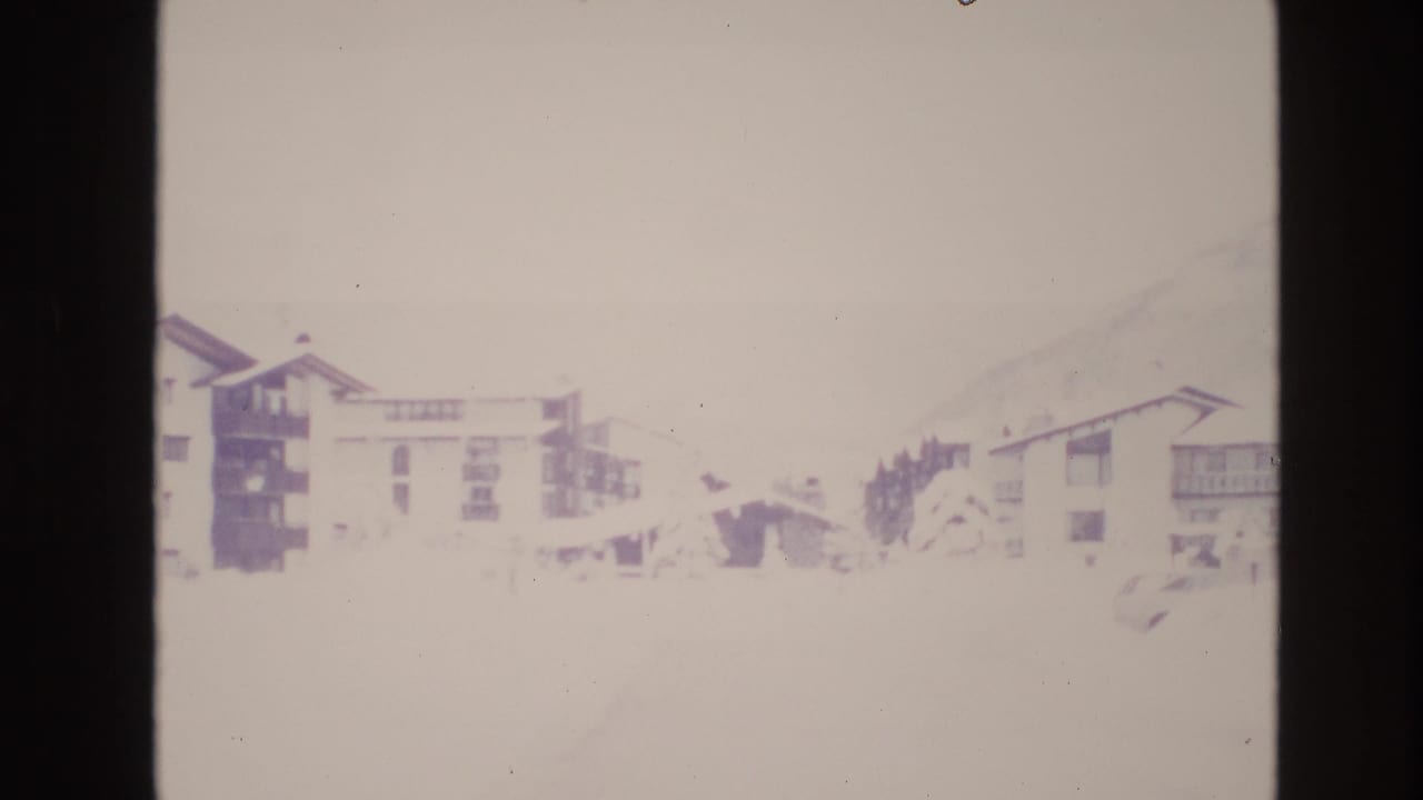 Faded 1974 8mm view of snow-covered resort buildings in Vail, Colorado, with a pale mountain slope behind them.