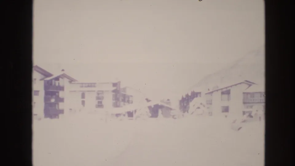 Faded 1974 8mm view of snow-covered resort buildings in Vail, Colorado, with a pale mountain slope behind them.