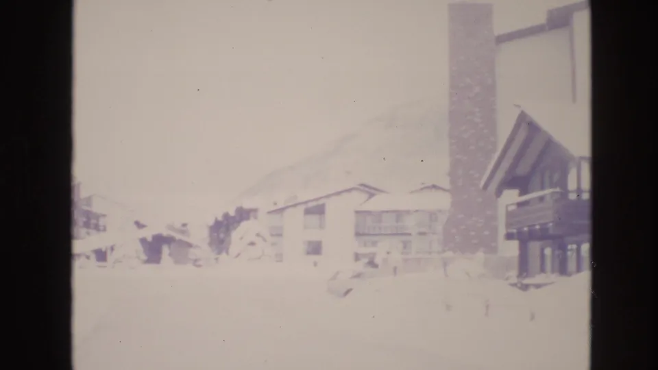 Soft, overexposed 8mm frame from Vail showing resort buildings, heavy snow, and a tall chimney-like structure near the lodging.