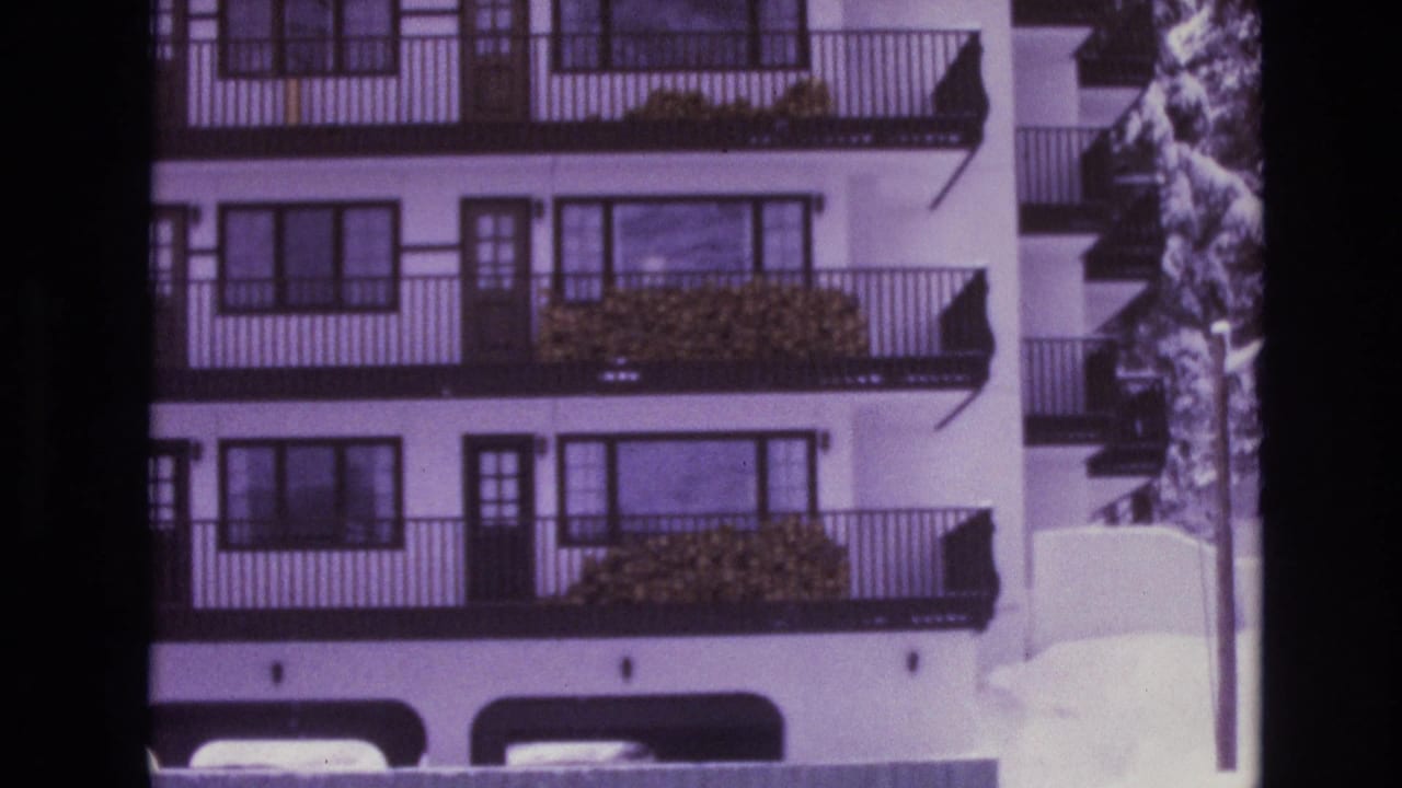 1974 Vail, Colorado home-movie frame showing a snow-covered resort building with stacked balconies, dark railings, and a purple 8mm color shift.