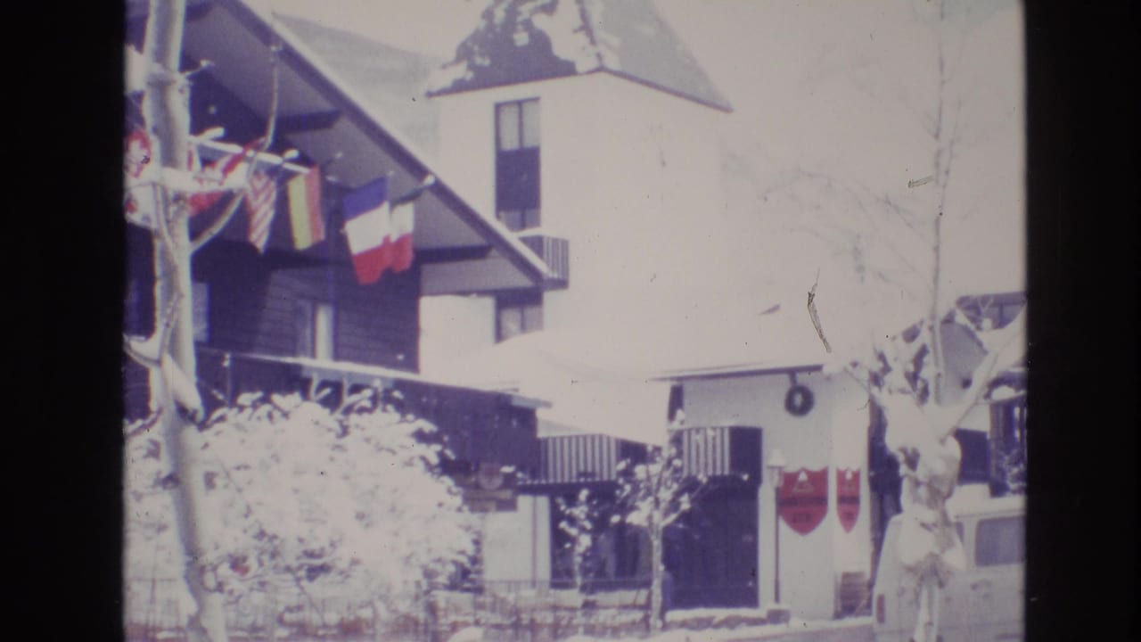 1974 Vail, Colorado frame of a bright, snow-covered alpine hotel facade with flags hanging from the eaves and the tower rising above the roof.