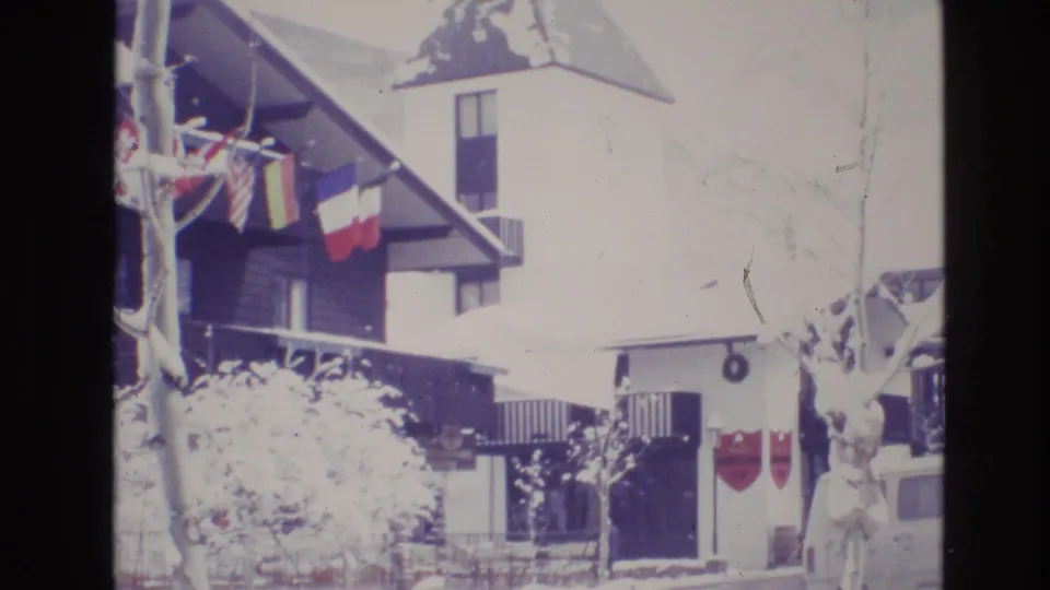 1974 Vail, Colorado frame of a bright, snow-covered alpine hotel facade with flags hanging from the eaves and the tower rising above the roof.