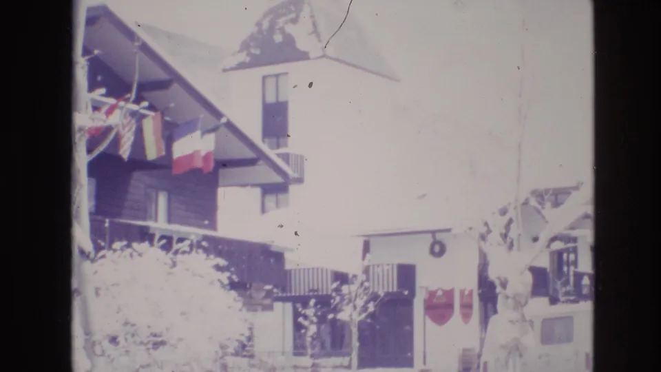1974 Vail, Colorado 8mm frame showing an overexposed snowy hotel exterior with a tower, international flags, bare tree branches, and the entrance area partly visible.
