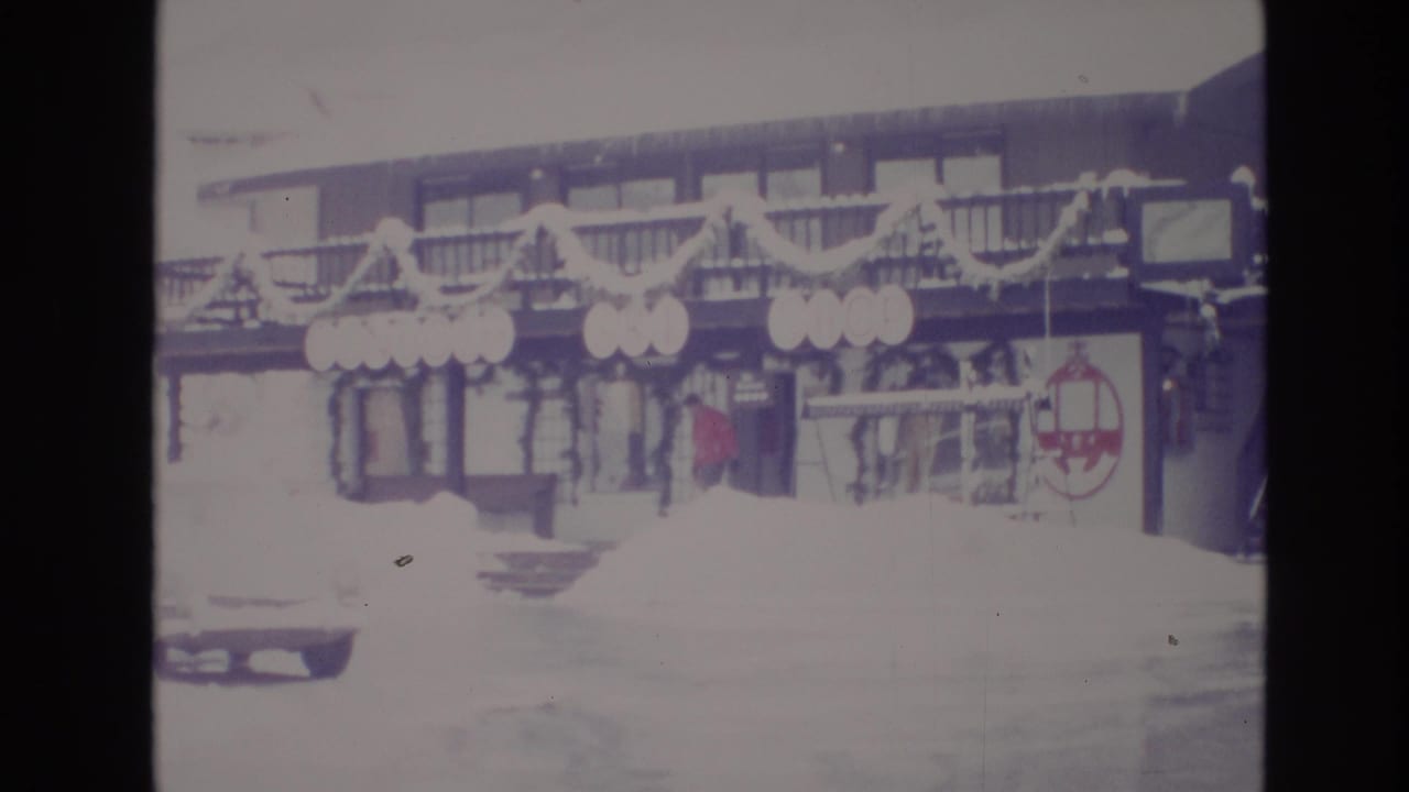 Faded 1974 home-movie frame from Vail, Colorado showing a snow-covered resort frontage decorated with garlands and circular signs.