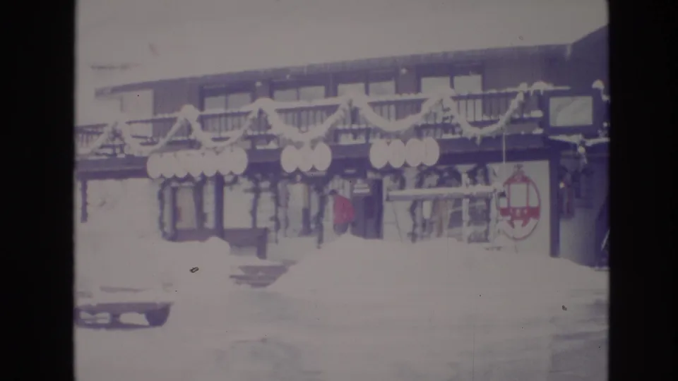 Faded 1974 home-movie frame from Vail, Colorado showing a snow-covered resort frontage decorated with garlands and circular signs.