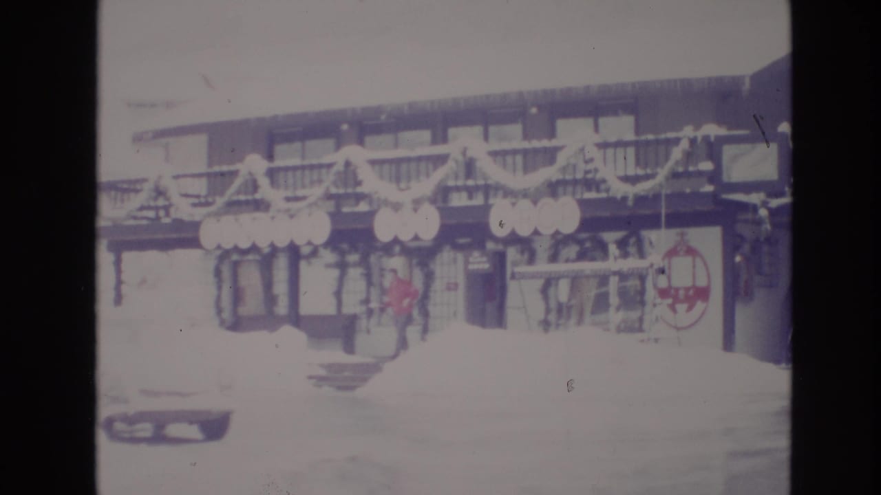 A 1974 Vail resort exterior appears through faded Super 8 color, with snow on the ground and a red-jacketed visitor near the entrance.