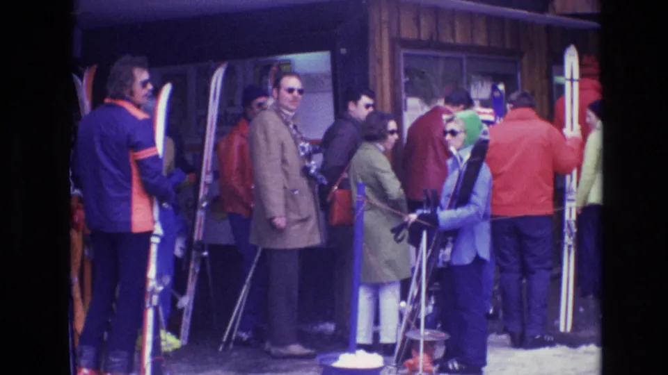 A dense line of Vail resort visitors in 1974 stands with skis and poles, showing colorful cold-weather clothing and casual home-movie framing.