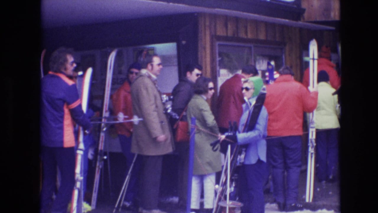 In Vail, Colorado in 1974, adults in bright winter coats and sunglasses stand in a queue outside a wooden ski lodge with skis and poles.