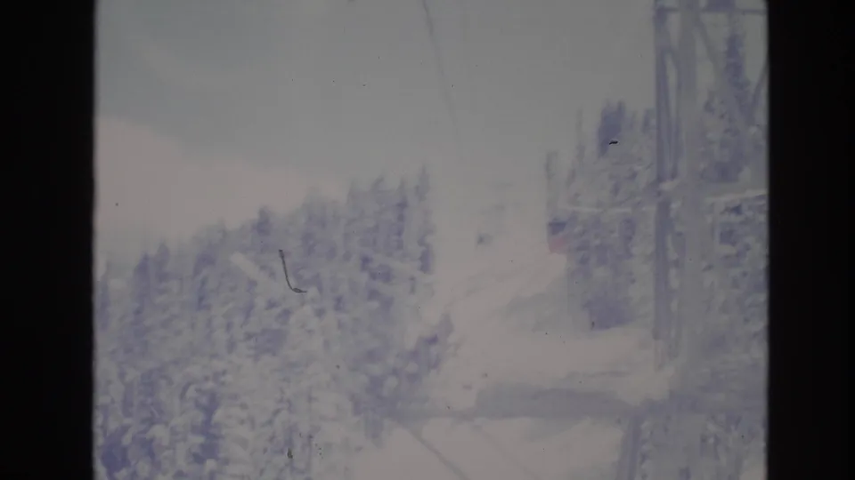 A faded 8mm frame shows ski-lift cables crossing a snowy evergreen slope at Vail, Colorado, with a small structure or building edge visible to the right.