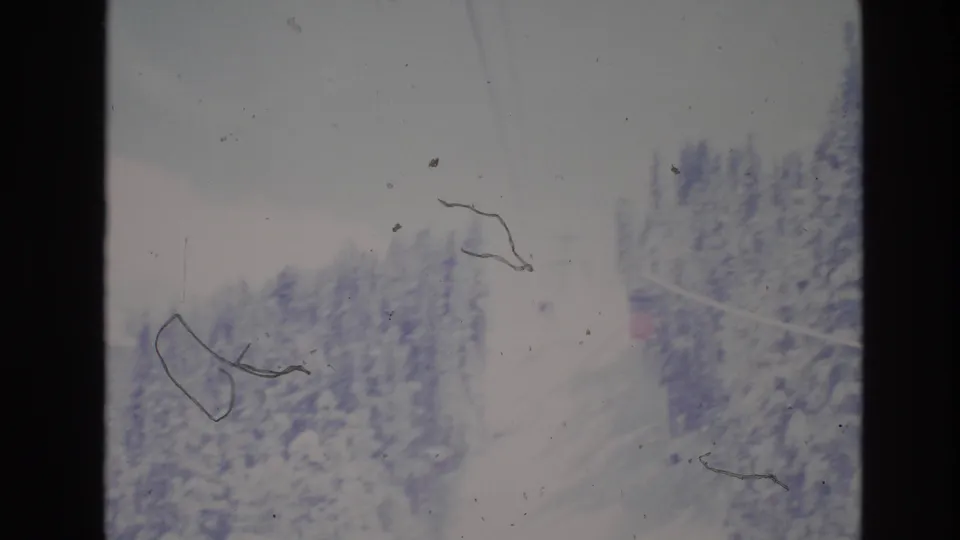 The 8mm frame looks across a snow-covered evergreen slope in the Vail ski area, with a small red detail near the edge and prominent surface marks from the film scan.