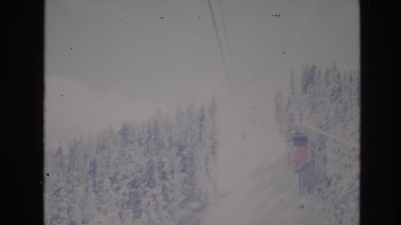 1974 Vail, Colorado 8mm frame showing snowy evergreen trees, faint ski lift cables, and a distant lift structure in a winter resort landscape.