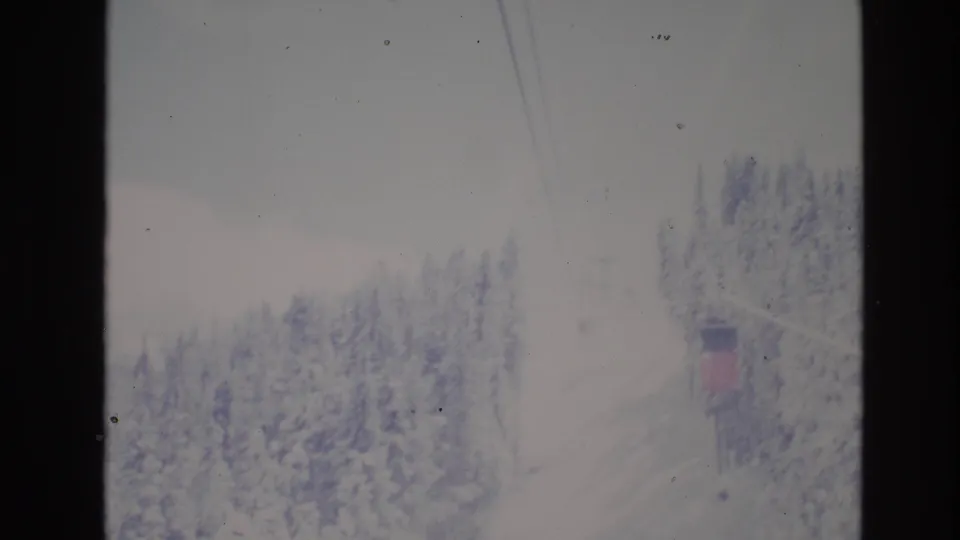 1974 Vail, Colorado 8mm frame showing snowy evergreen trees, faint ski lift cables, and a distant lift structure in a winter resort landscape.