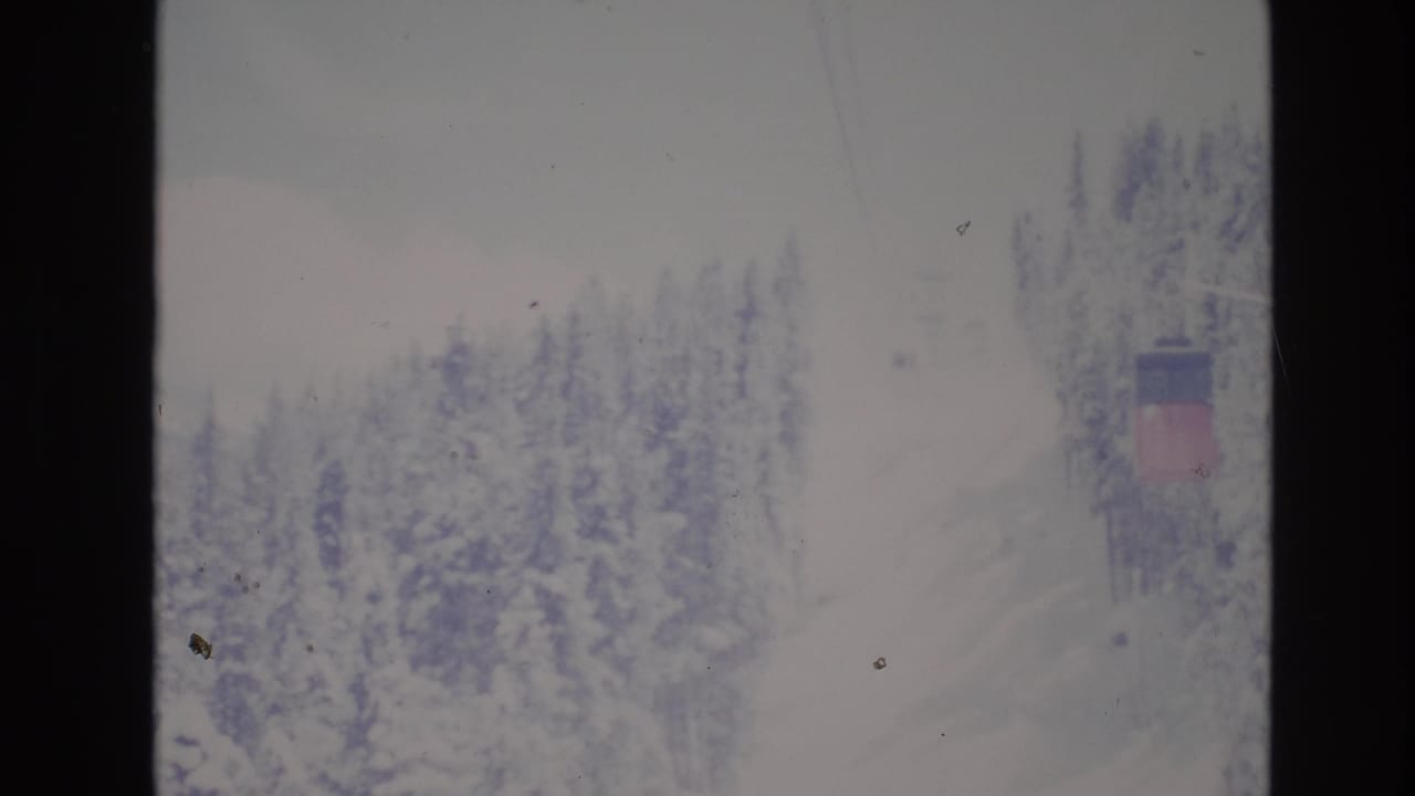 Snowy treeline with ski lift cables and a small distant lift structure.