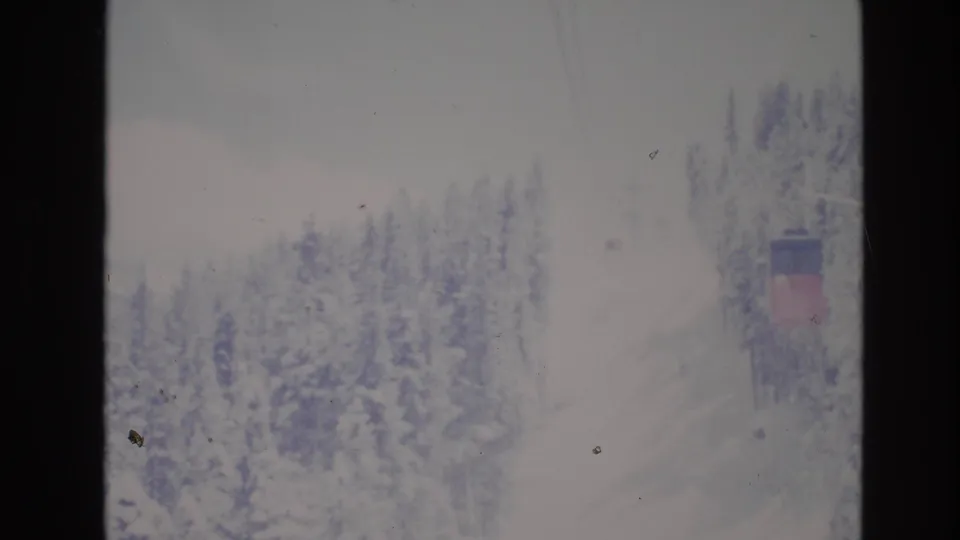1974 Vail, Colorado 8mm frame with a snowy treeline, faint overhead lift cables, and a small lift structure near the edge of the frame.