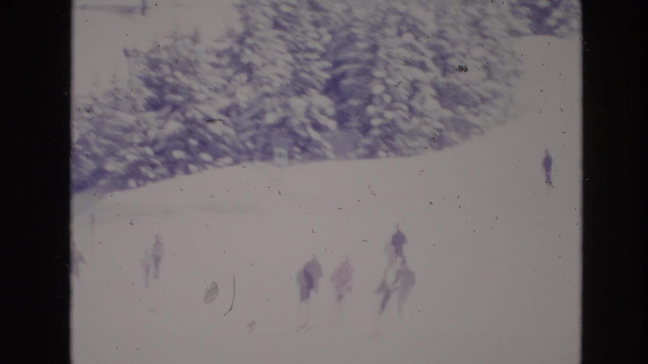 1974 Vail, Colorado 8mm frame showing distant skiers moving across an overexposed snowy slope below snow-covered evergreens.