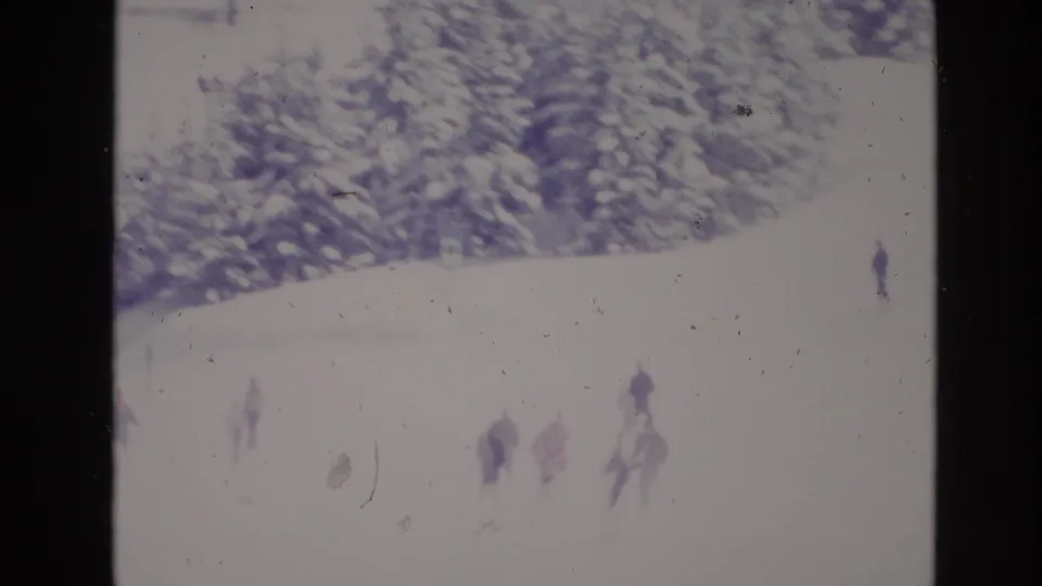 1974 Vail, Colorado 8mm frame showing distant skiers moving across an overexposed snowy slope below snow-covered evergreens.