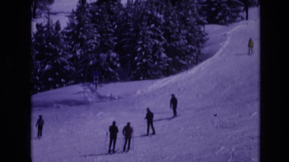 1974 Vail, Colorado frame with several skiers spread across a snowy resort slope bordered by dense evergreen trees.