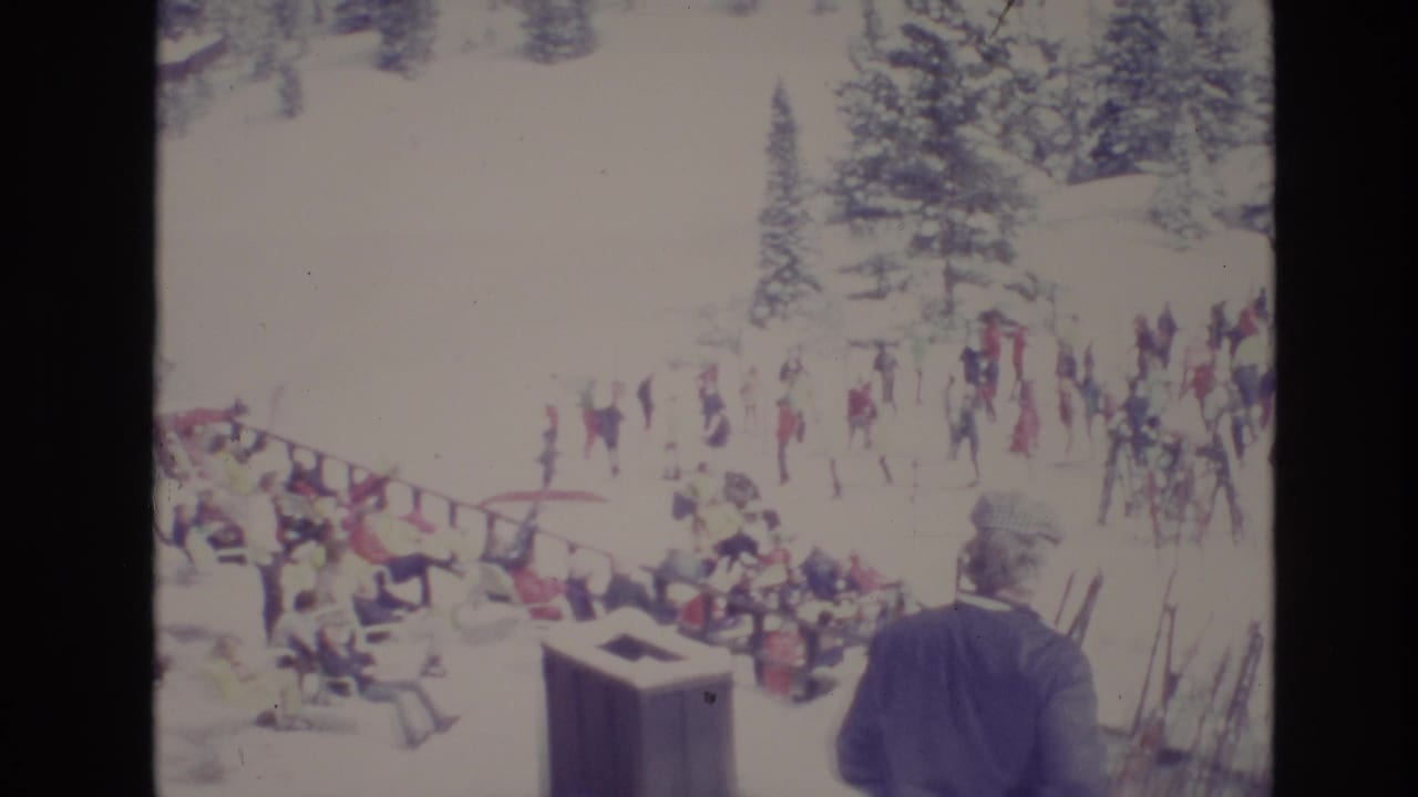 Crowded ski area with a man standing near upright skis in the foreground.