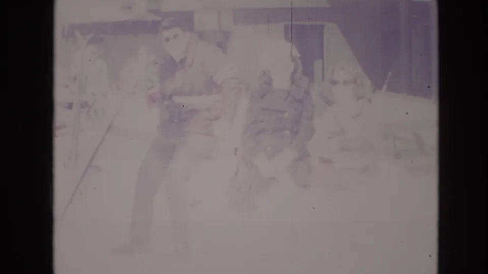 Overexposed 1974 Vail resort frame showing a man holding or standing beside skis near other visitors and a building wall in the snowy base area.