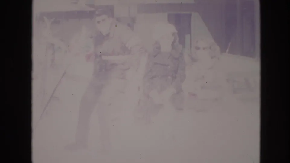 1974 Vail home-movie frame showing adults in winter coats standing in overexposed snow near a lodge or resort building.