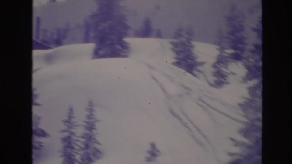 Snowy mountain slope in Vail with evergreen trees and visible tracks, filmed with soft focus and faded color on 8mm film.