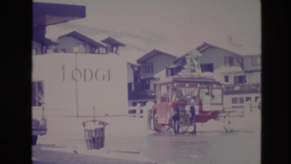 Vail lodge-area street scene with snowy buildings, a visible lodge sign, and a red horse-drawn carriage parked outside.