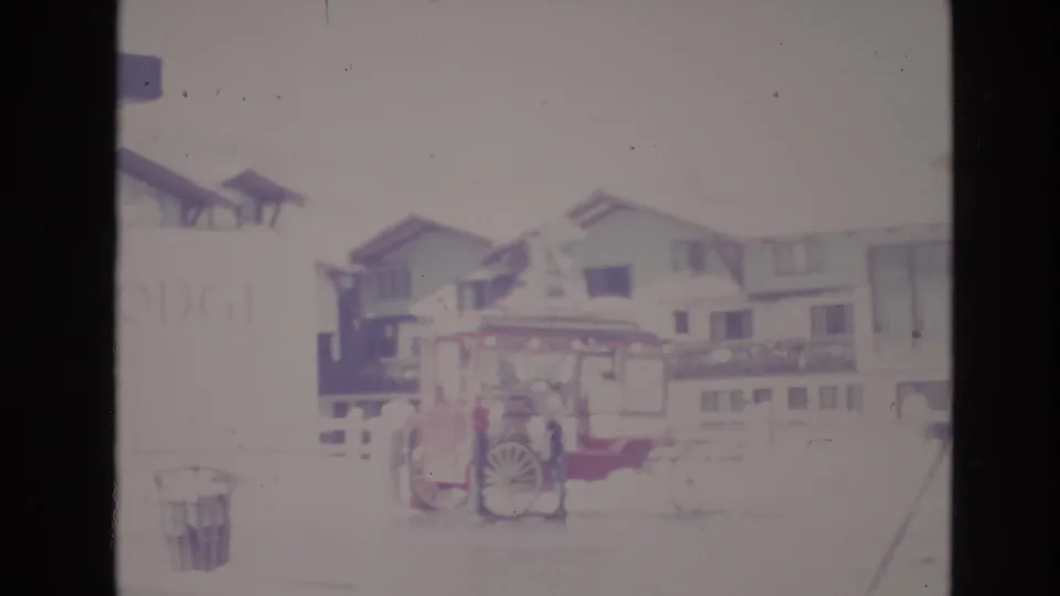 Soft, overexposed 1974 Vail, Colorado frame showing the red cart parked in front of snowy resort buildings with a faint sign at left.