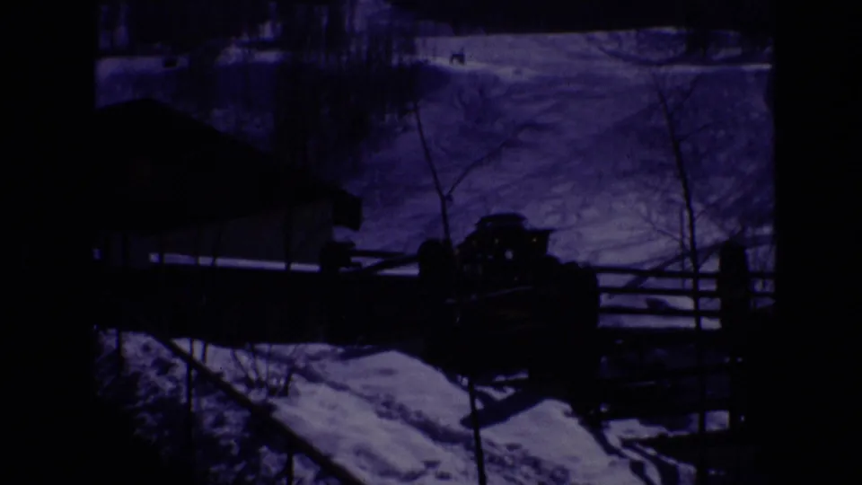 1974 Vail, Colorado home-movie frame showing a snow-covered resort area, a low modern building, wooden fencing, and a parked vehicle under heavy blue-purple tint.