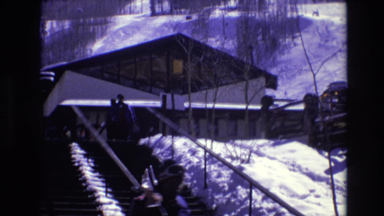 1974 Vail, Colorado 8mm frame showing a snow-covered stairway and railings leading toward a modernist hilltop resort building with winter visitors nearby.