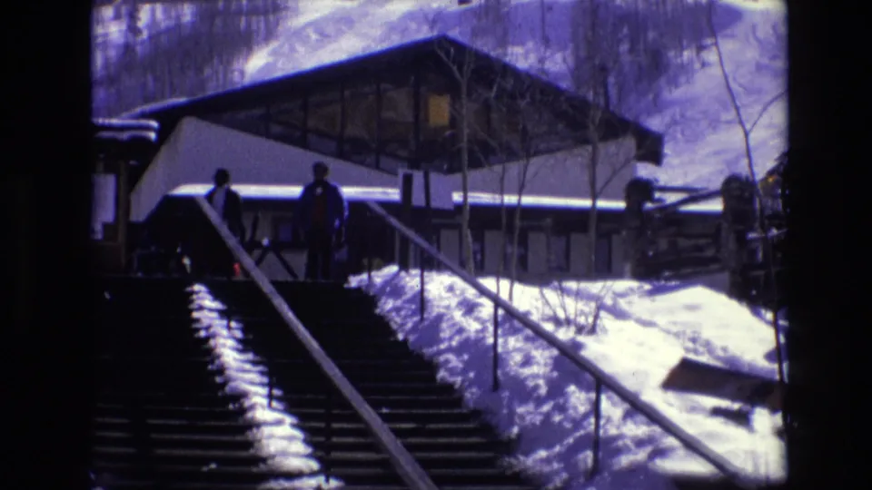 1974 Vail, Colorado frame with two distant winter visitors near the top of a long outdoor stairway beneath a snow-covered modernist building.