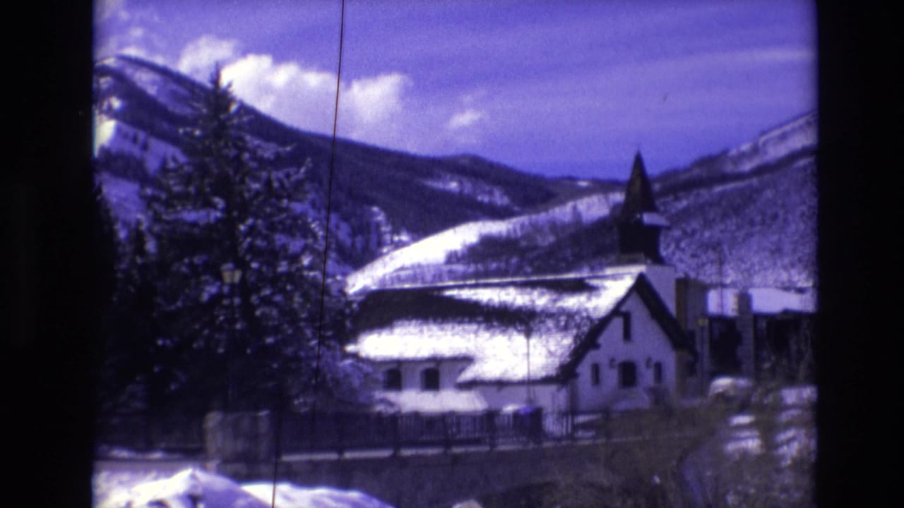 1974 Vail, Colorado 8mm frame showing a snow-covered church with a dark steeple, evergreen trees, and mountain slopes in the background.