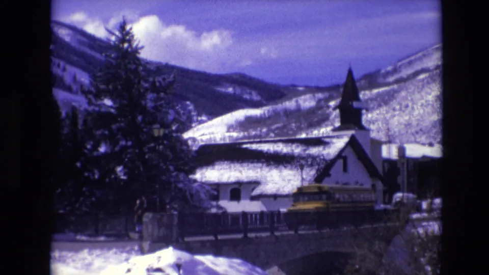 1974 Vail, Colorado frame showing a yellow school bus near a snow-covered white steepled building, with evergreen trees and mountain slopes in the background.