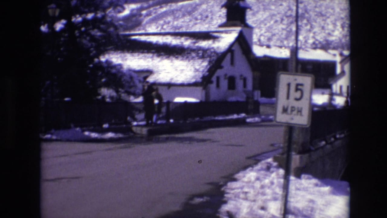 Vail, Colorado winter street view from 1974 home-movie footage, showing a snow-covered road, a church-like building with a steeple, pedestrians, and a school bus near a bridge.