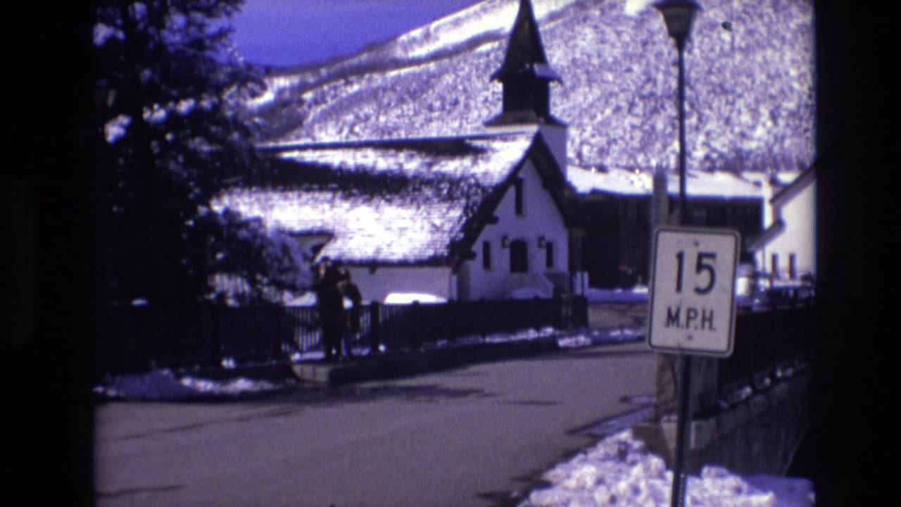 1974 Vail, Colorado street scene with a 15 M.P.H. sign in the foreground, pedestrians on a snow-lined road, and a steepled church-like building below snowy slopes.