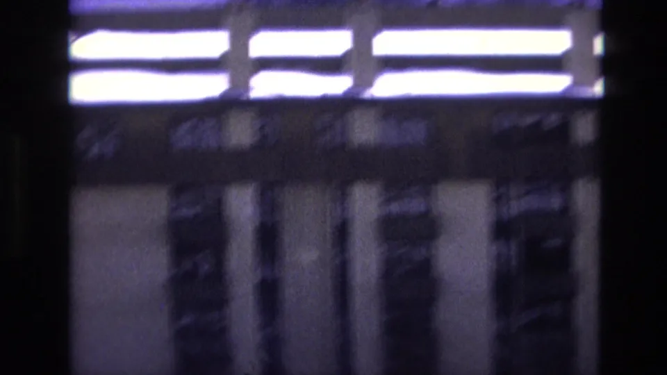 Soft 8mm frame from the Vail winter clip showing a blurred building facade with bright horizontal architectural or sign elements and dark vertical window shapes.