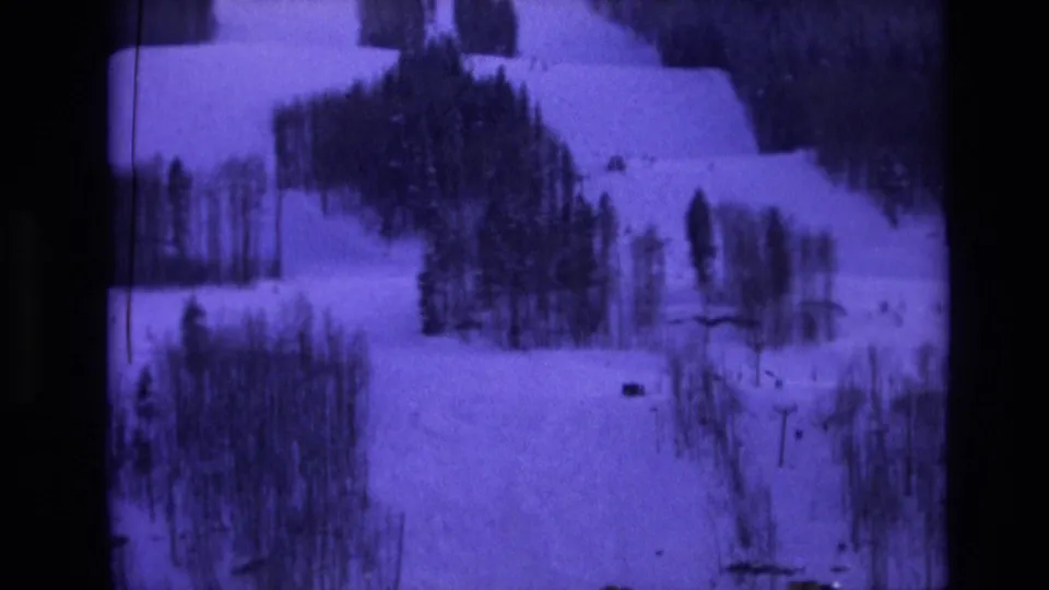 1974 Vail-area home-movie frame showing a snow-covered hillside broken by evergreen stands and distant dark shapes.