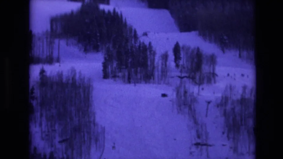 Purple-tinted 8mm frame from Vail, Colorado in 1974 showing a winter hillside with dense evergreen stands and open snowfields.