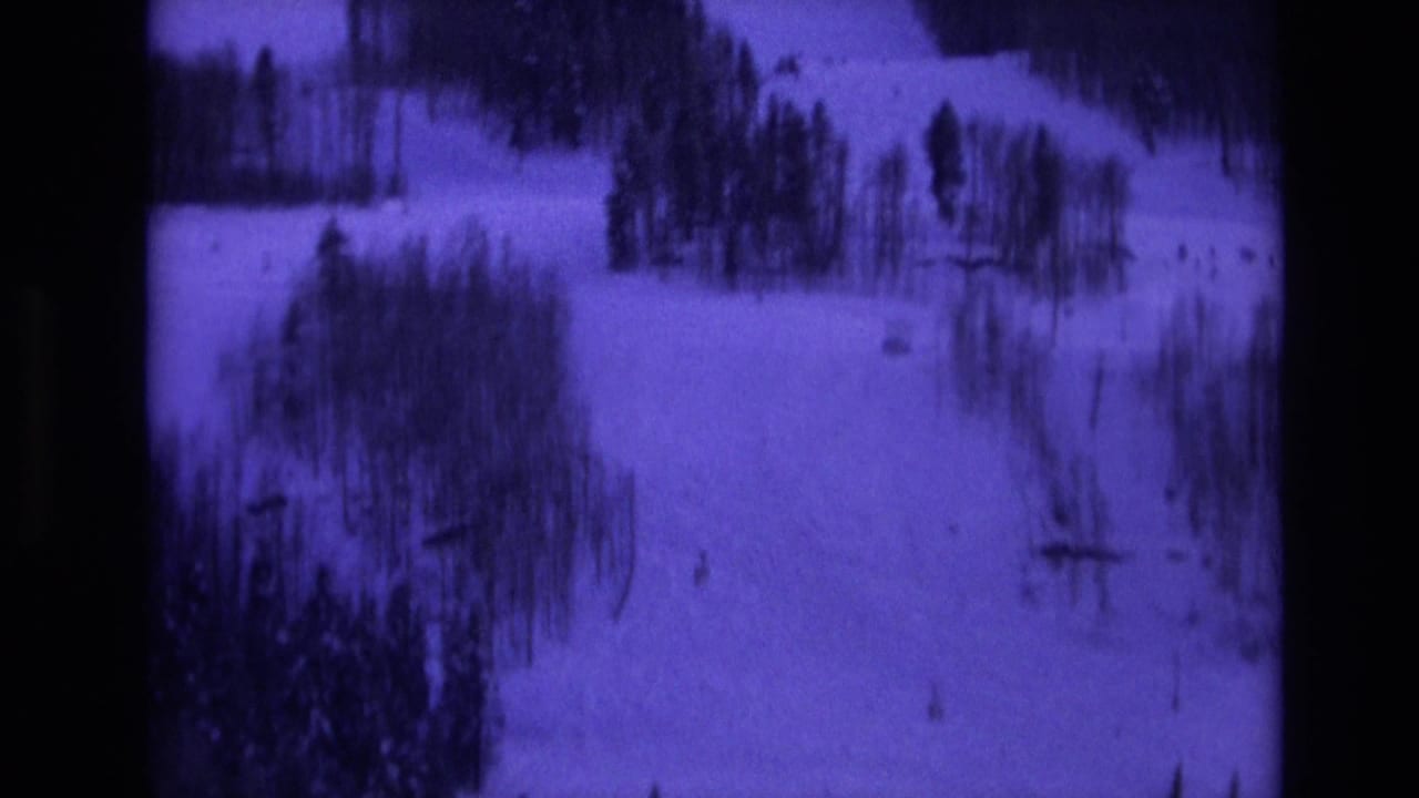 Snow-covered ski slope with trees, tracks, and distant lift structures.